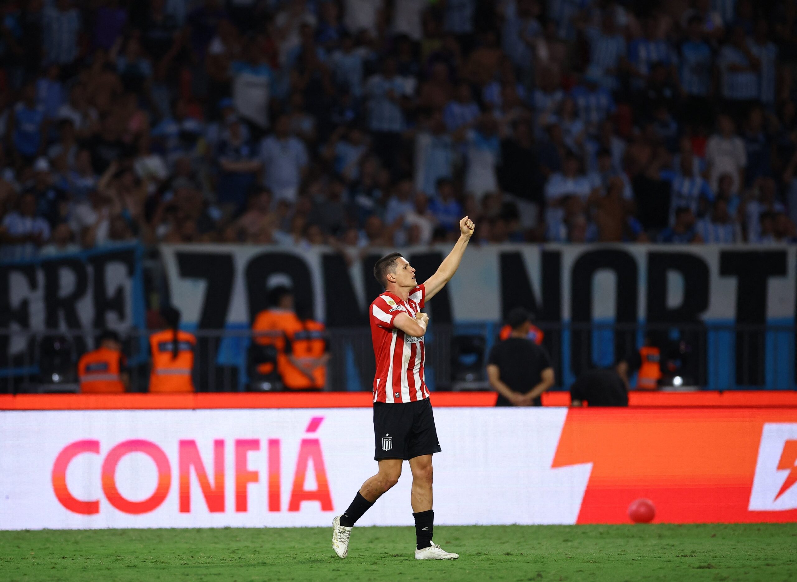 Jogador do Estudiantes comemora em campo diante da torcida no Alt, título e descrição.